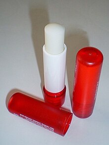 Цилиндрический кусок почти белой помады, закреплённый в пластмассовой цилиндрической упаковке.
